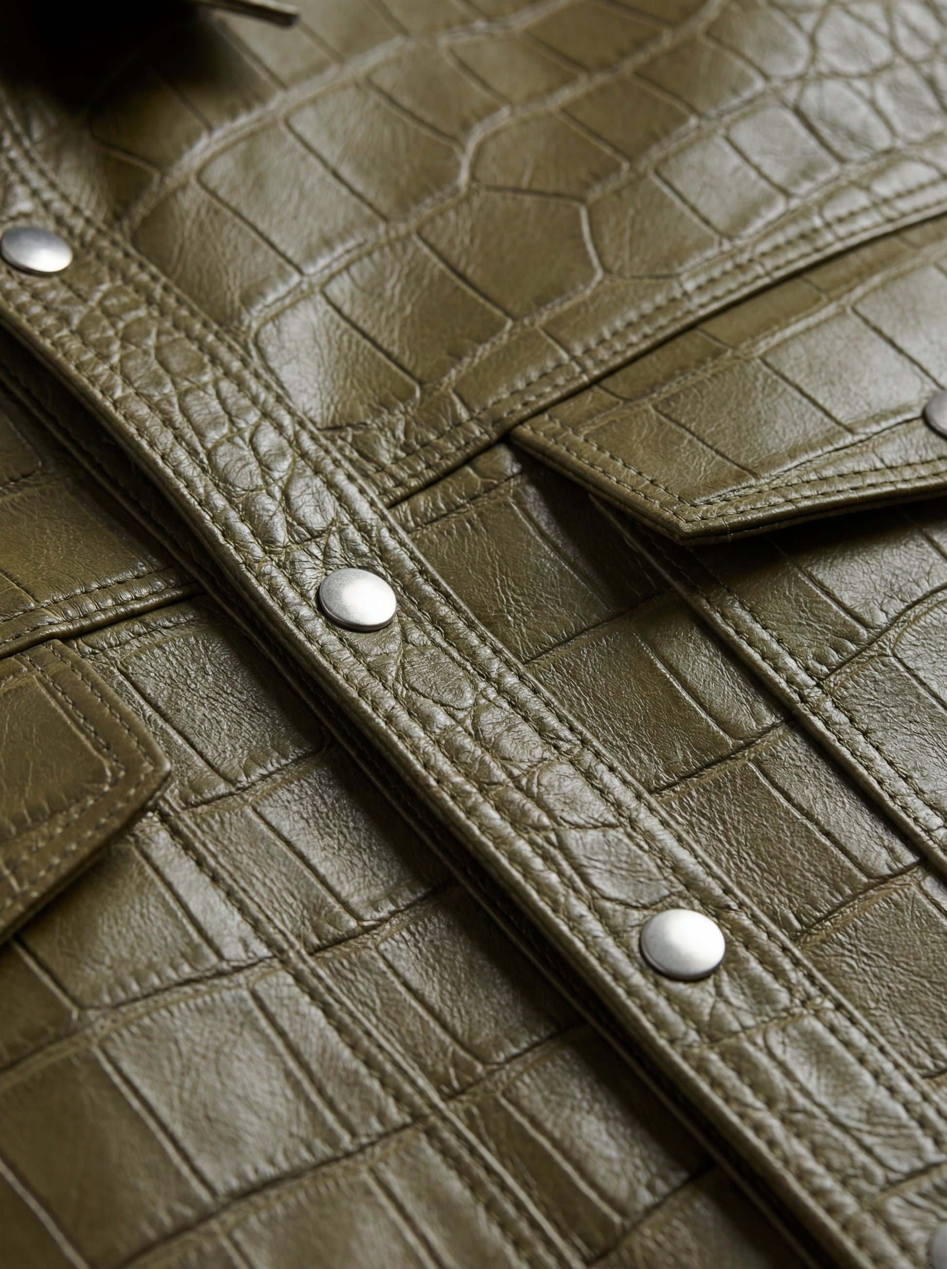 Macro shot of detailed crocodile-embossed leather texture and silver snap button detail on western shirt. The Roman by Maverick Jacket.