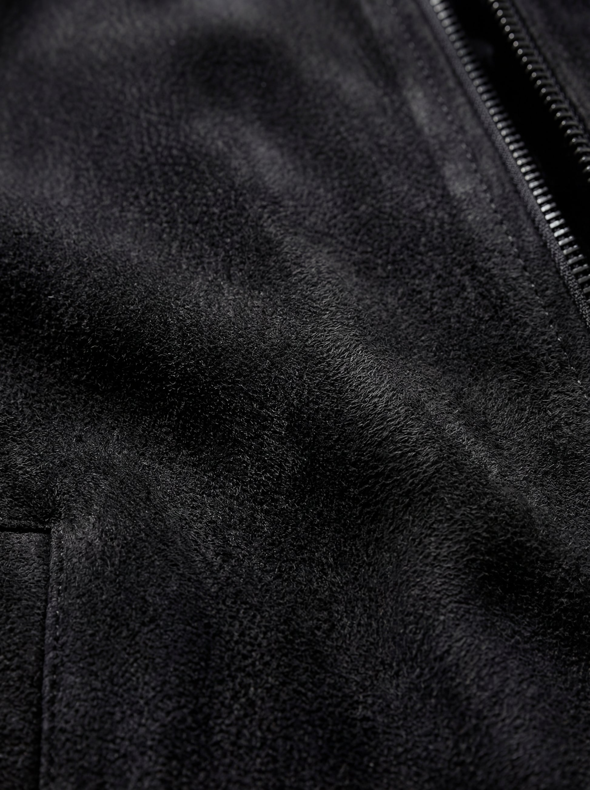 Macro shot of soft black suede texture and metal zipper hardware on bomber jacket. The Felix by Maverick Jacket.