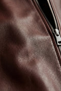 Macro shot of dark brown pebbled leather texture and silver zipper hardware on bomber jacket. The Ferran by Maverick Jacket.