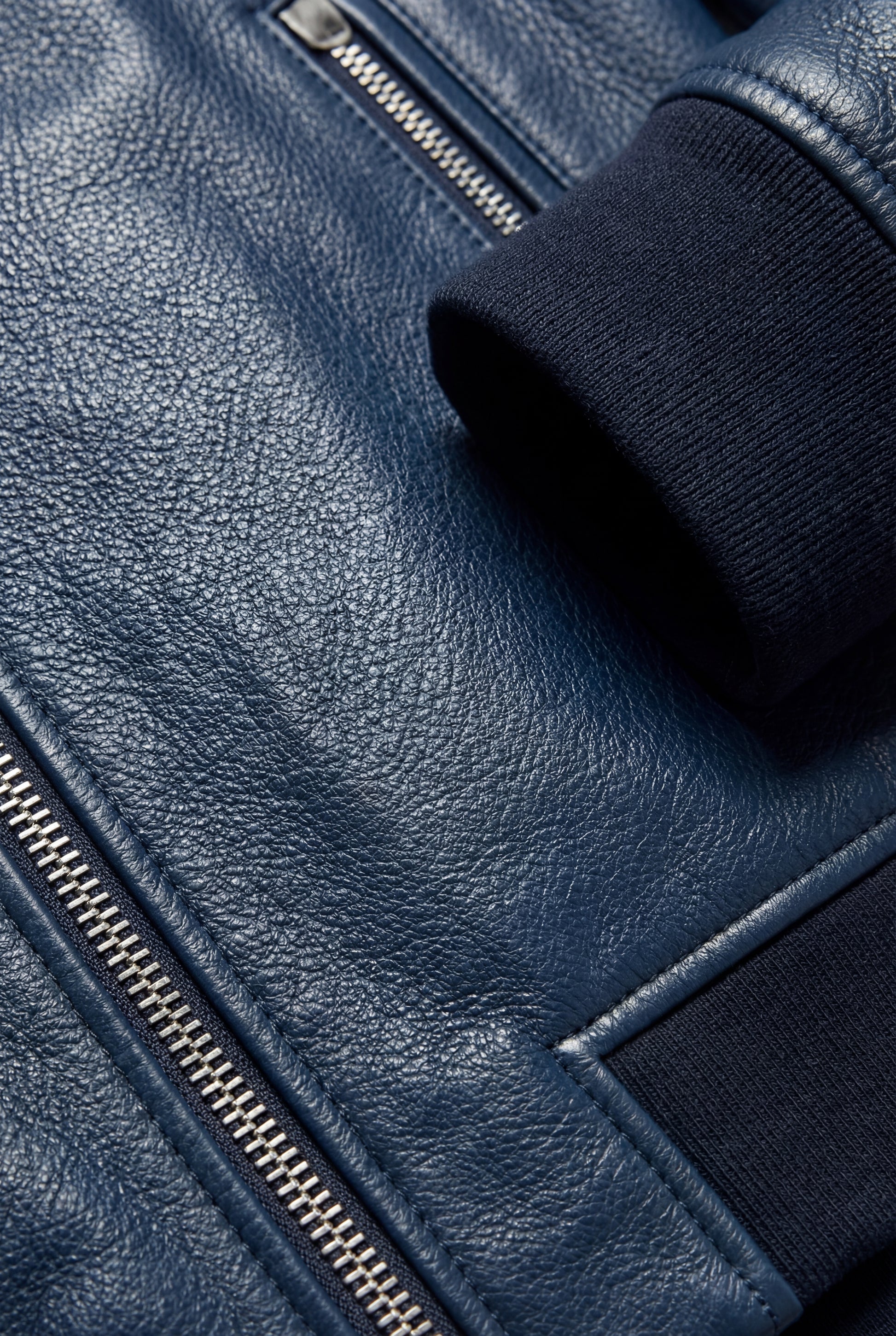Macro shot of navy blue pebbled leather texture and ribbed knit cuff detail on bomber jacket. The Solaro by Maverick Jacket.