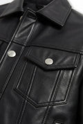Macro shot of black pebbled leather grain texture and silver button flap pocket detail on trucker jacket. The Veyron by Maverick Jacket.