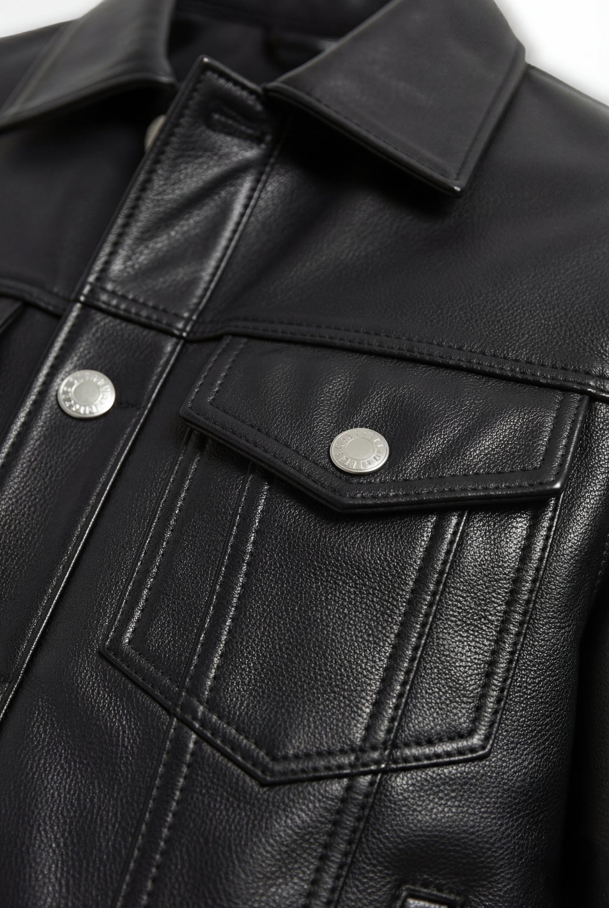 Macro shot of black pebbled leather grain texture and silver button flap pocket detail on trucker jacket. The Veyron by Maverick Jacket.