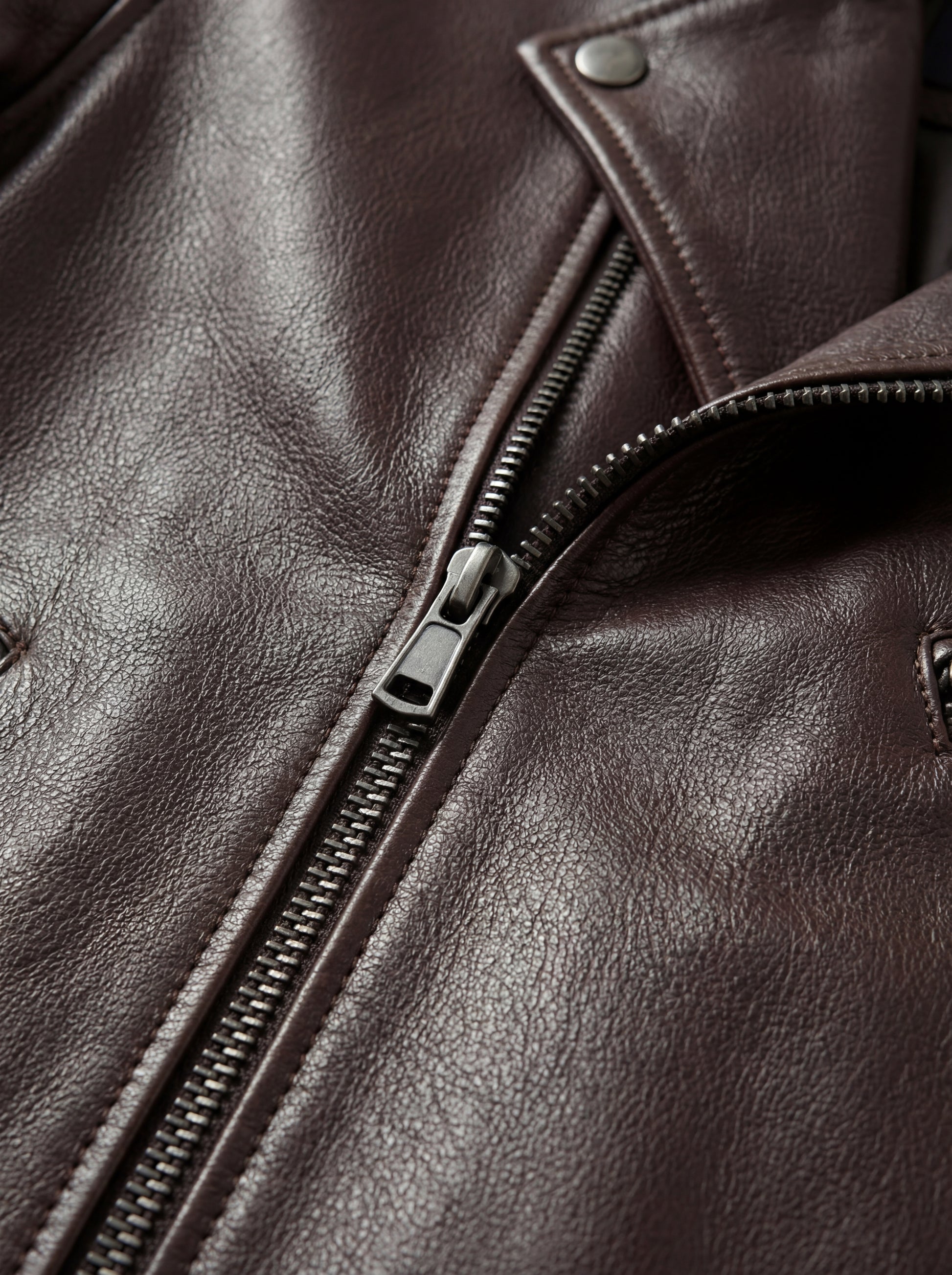 Macro shot of brown pebbled leather texture and silver metal zipper hardware on biker jacket. The Roadmaster by Maverick Jacket.