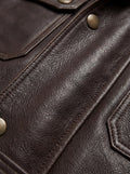 Macro shot of dark brown pebbled leather texture and antique brass snap button detail on field jacket. The Huntsman by Maverick Jacket.