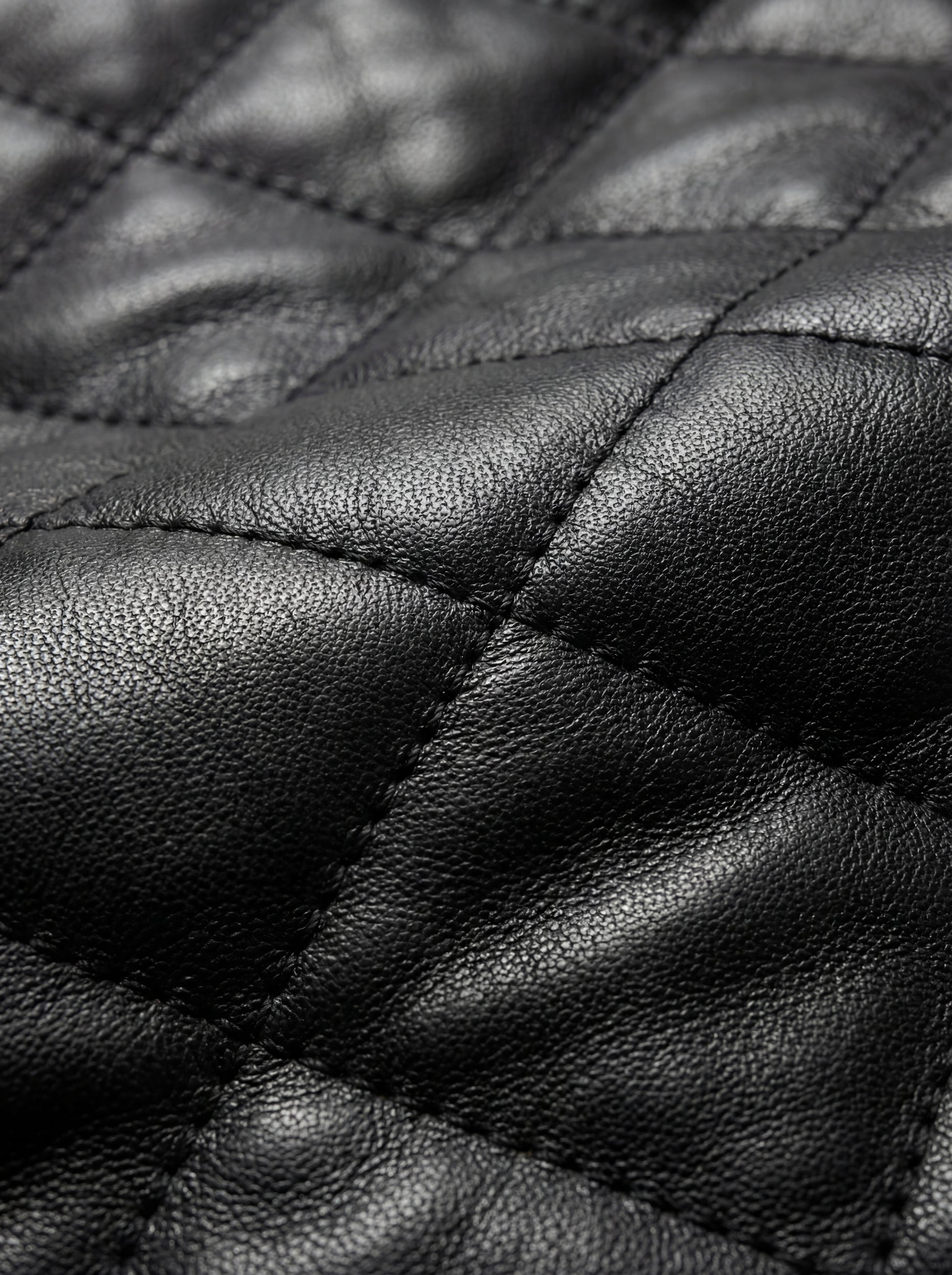 Macro shot of black leather texture and intricate diamond stitching detail on bomber jacket. The Nero by Maverick Jacket.