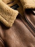 Macro shot of pebbled brown leather texture and thick cream shearling collar on aviator jacket. The Sterling by Maverick Jacket.