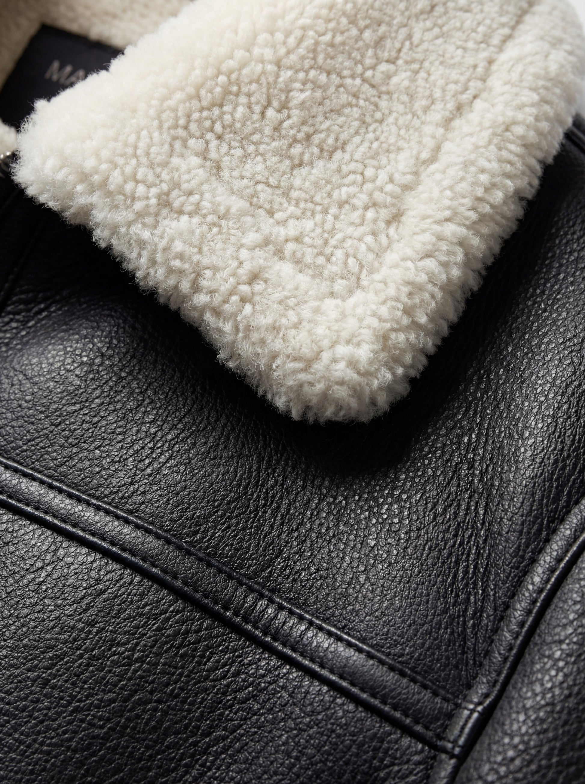 Macro shot of pebbled black leather texture and thick white shearling collar on bomber jacket. The Ronan by Maverick Jacket.