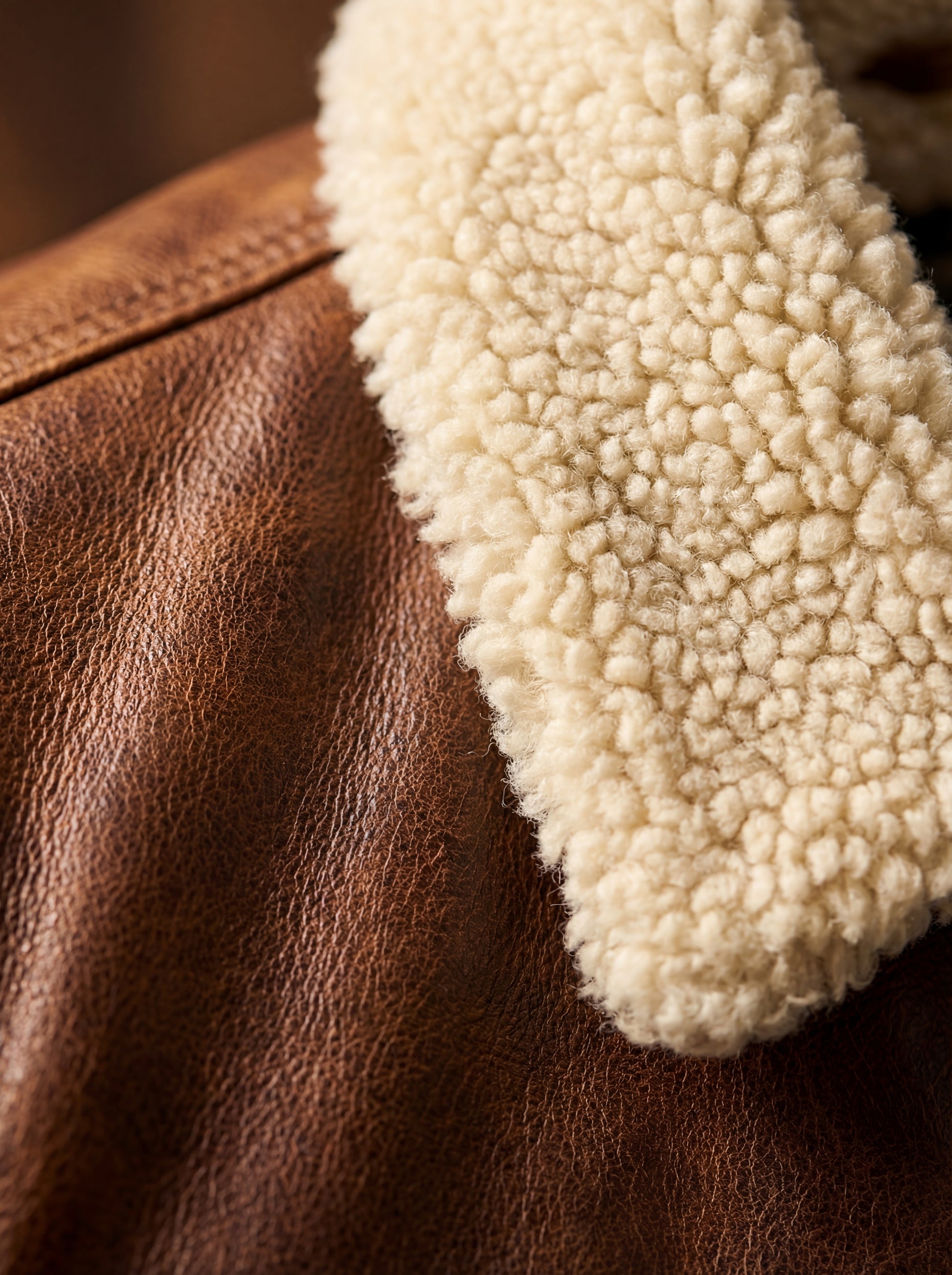 Macro shot of distressed brown leather grain and thick cream shearling collar texture on trucker jacket. The Wyatt by Maverick Jacket.