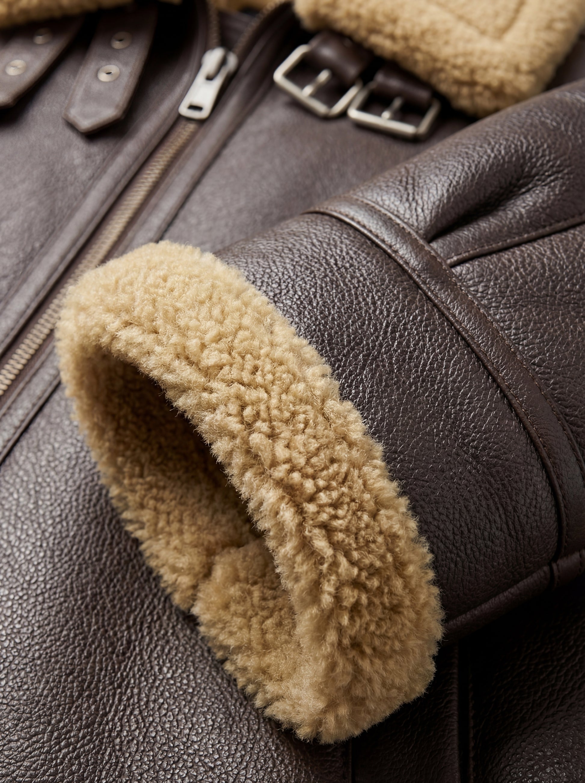 Macro shot of pebbled dark brown leather texture and thick beige shearling cuff on aviator jacket. The Beckett by Maverick Jacket.