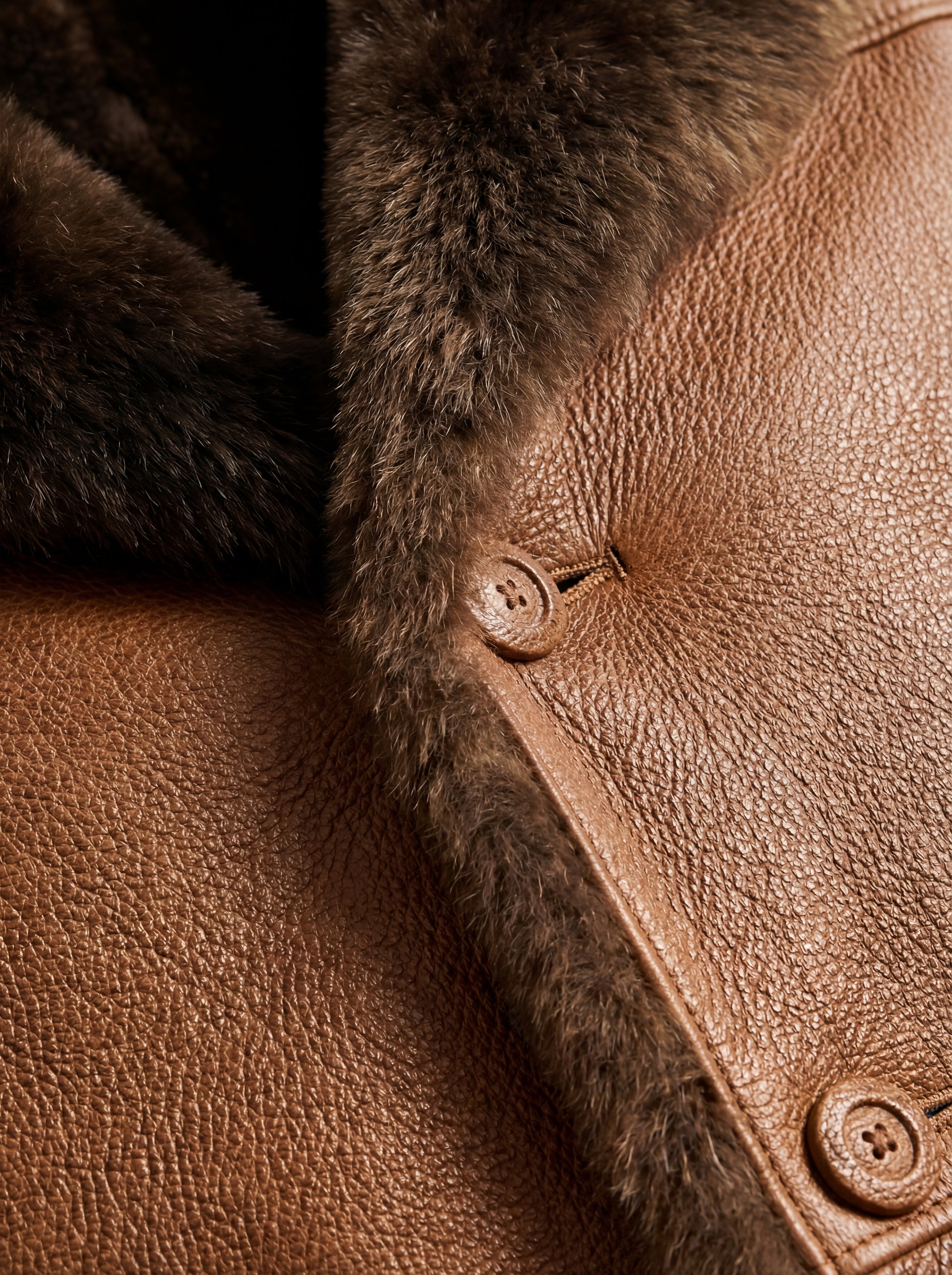 Macro shot of pebbled leather texture and button closure with dark shearling trim on coat. The Alistair by Maverick Jacket.