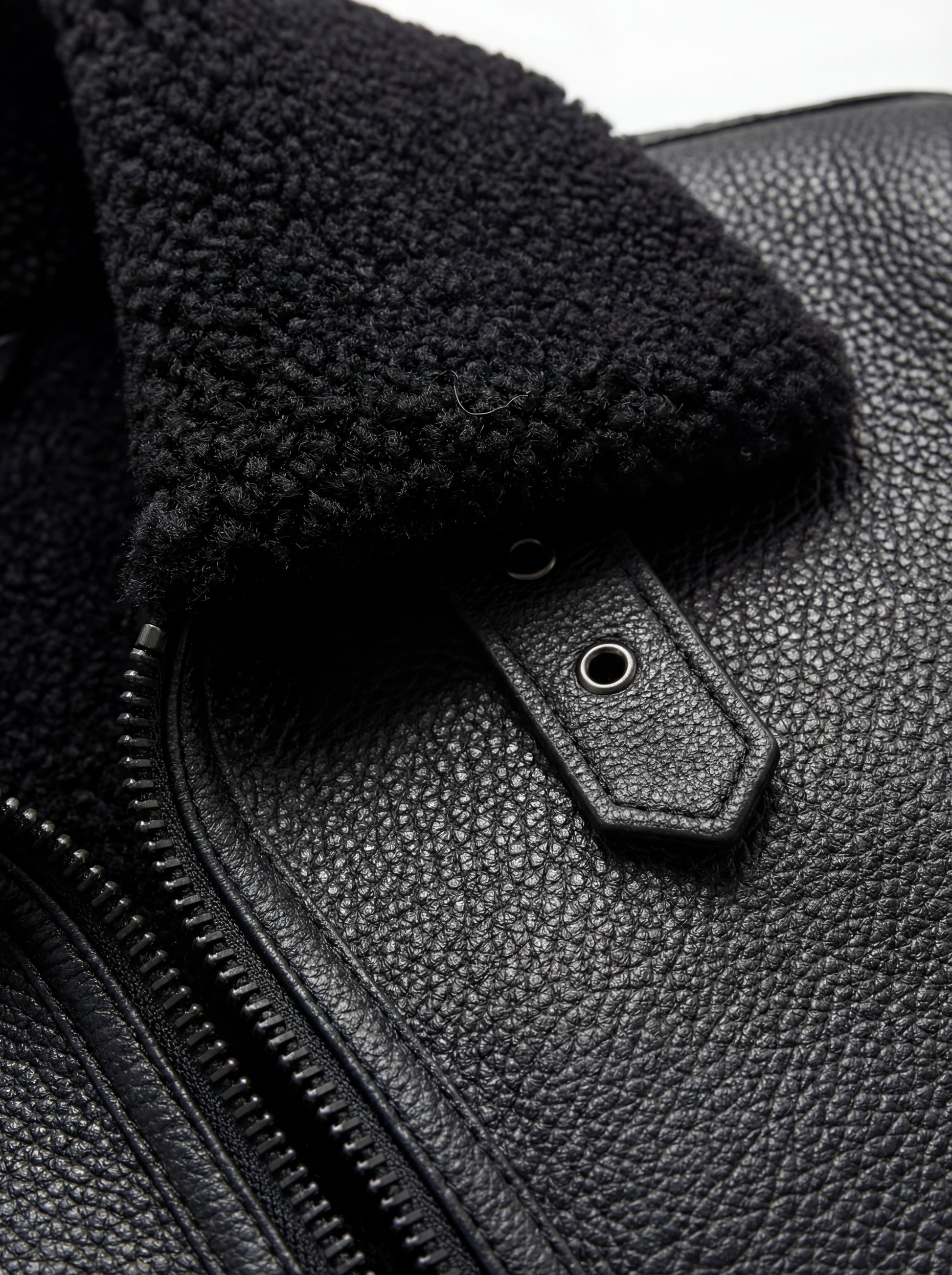 Macro shot of pebbled black leather texture and collar buckle hardware on jacket. The Zane by Maverick Jacket.