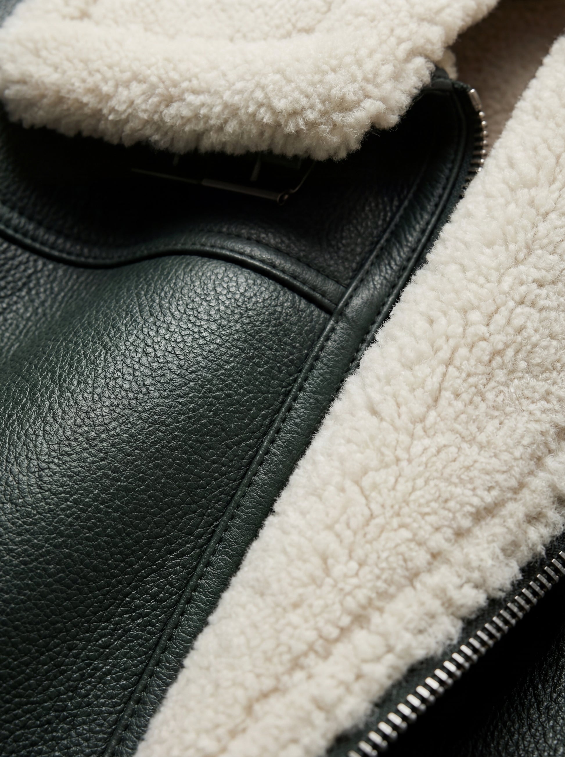 Macro shot of pebbled forest green leather texture and thick white shearling collar on aviator jacket. The Lorcan by Maverick Jacket.