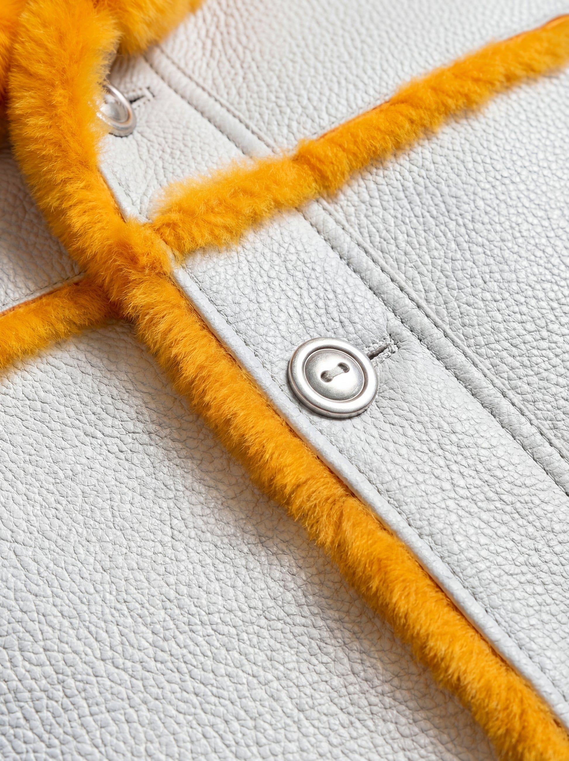 Macro shot of pebbled white leather texture and silver button detail on parka. The Axel by Maverick Jacket.