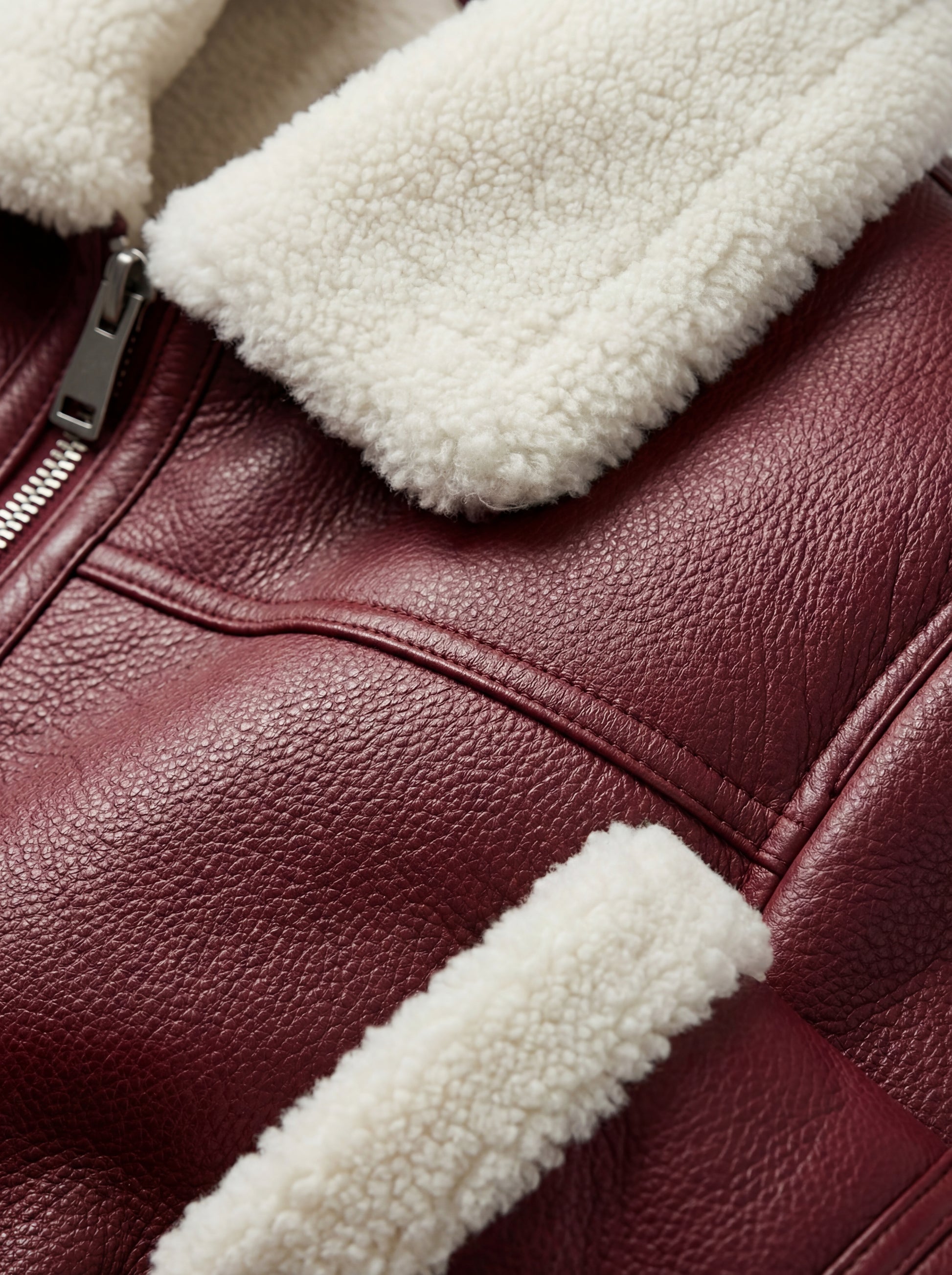 Macro shot of pebbled burgundy leather texture and thick white shearling collar on aviator jacket. The Cormac by Maverick Jacket.