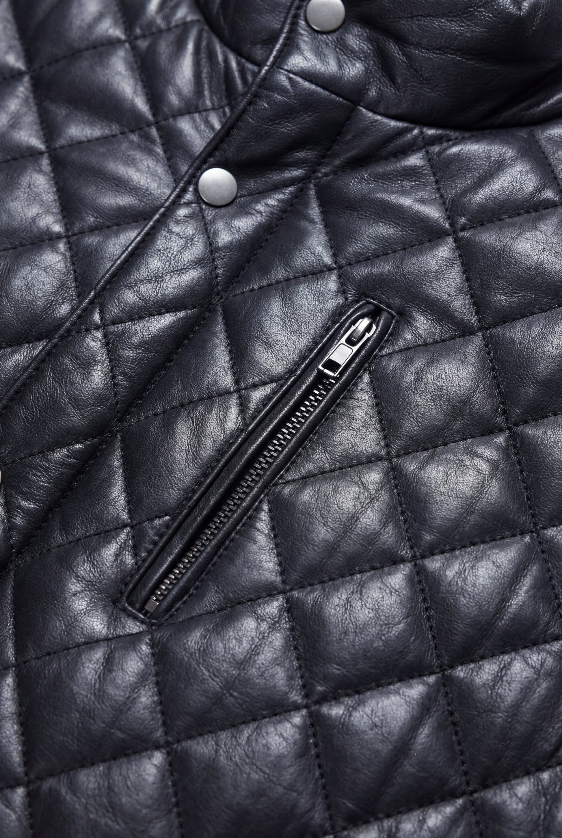 Macro shot of diamond quilted leather texture and silver zipper hardware on vest. The Graham by Maverick Jacket.