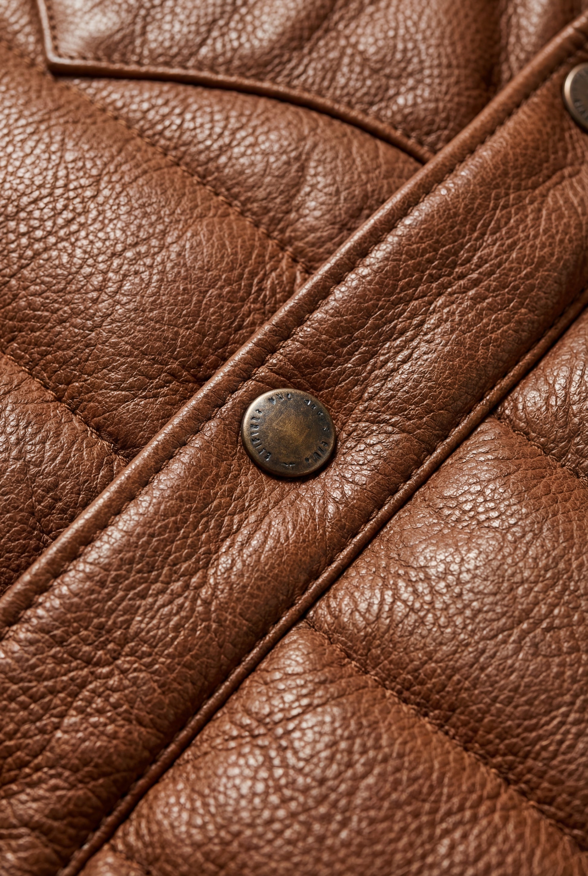 Macro shot of tan suede yoke texture contrasting with nylon puffer body and snap buttons on vest. The Nash by Maverick Jacket.