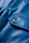 Macro shot of grained blue leather texture and embossed gold button detail on cargo pocket. The Enzo by Maverick Jacket.