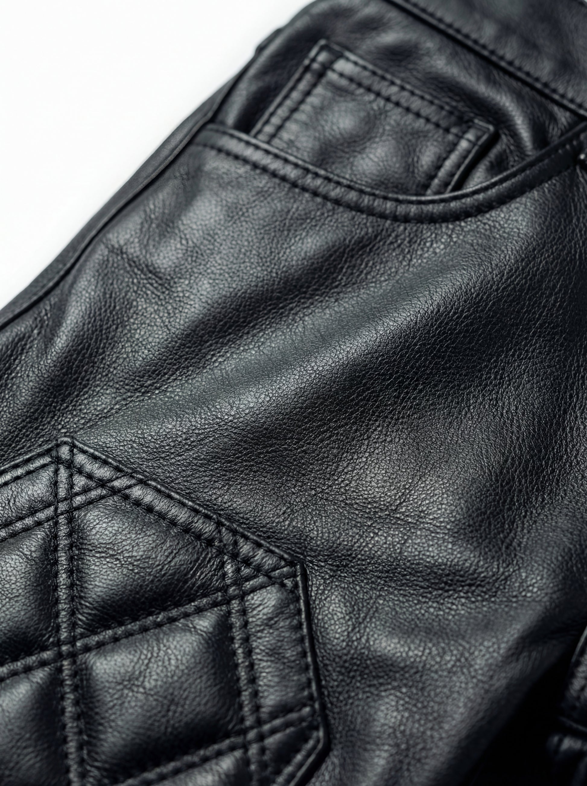 Macro shot of black pebbled leather texture and diamond quilting stitch detail on moto pants. The Jett by Maverick Jacket.