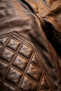 Macro shot of distressed brown leather grain and diamond quilting stitches on pants. The Nolan by Maverick Jacket.
