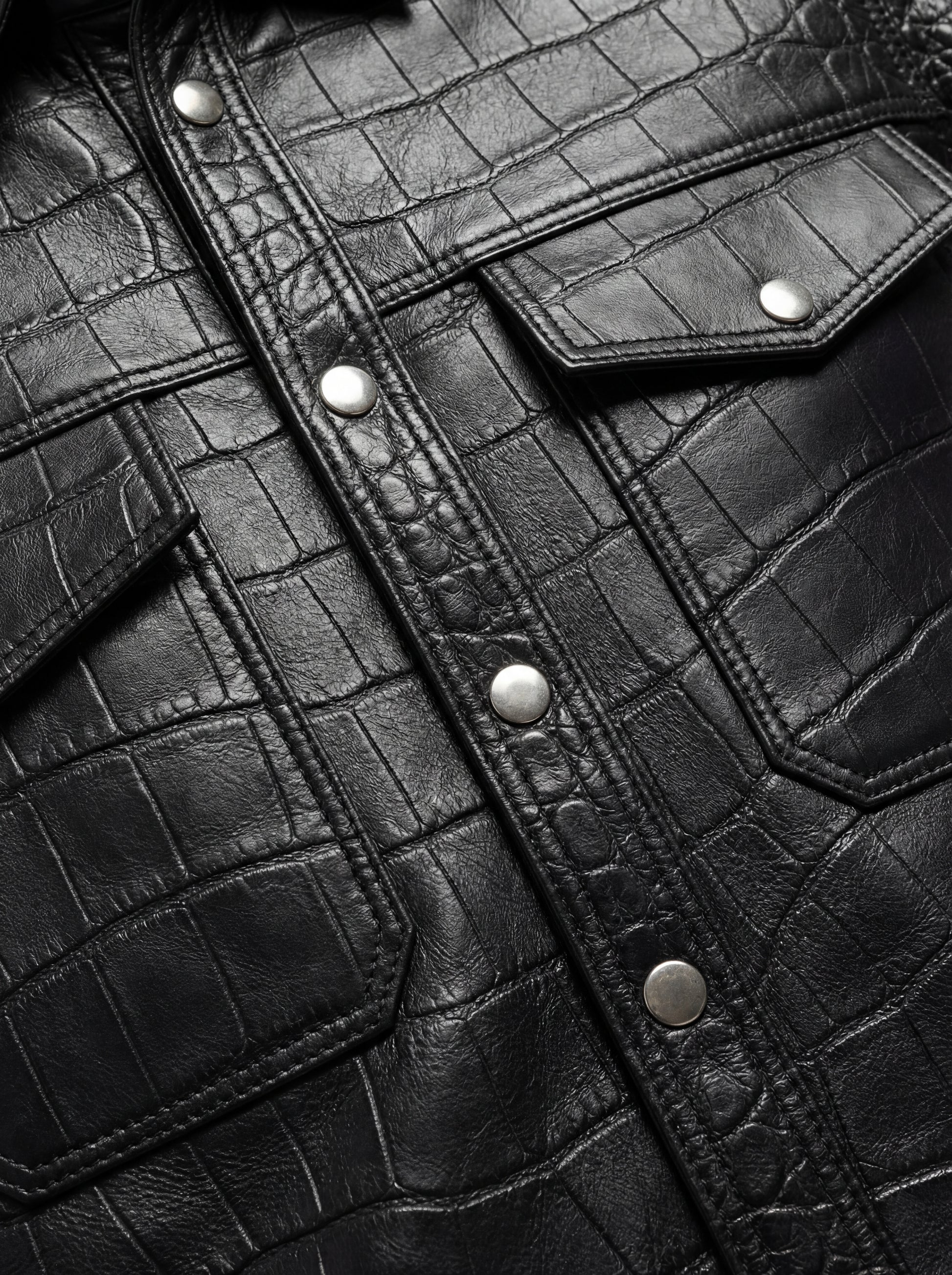 Macro shot of crocodile-embossed leather texture and silver snap button detail on shirt. The Damien by Maverick Jacket.