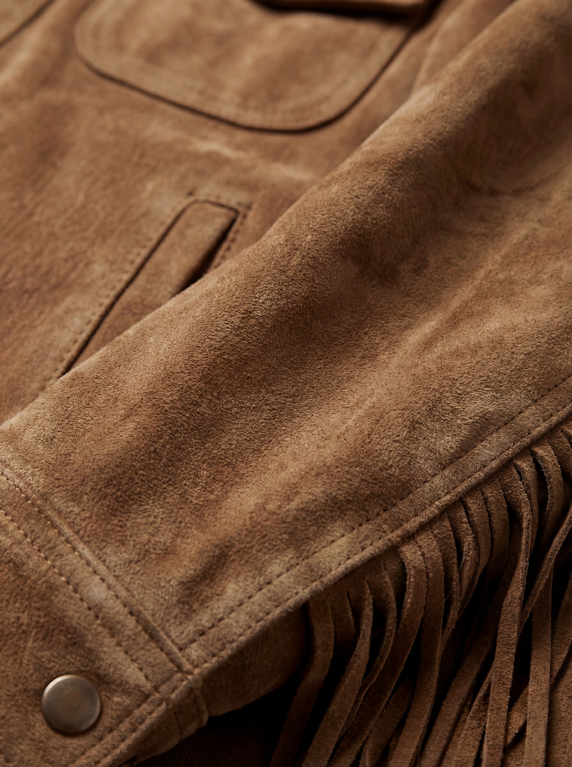 Macro shot of soft tan suede texture and fringe strand detailing on jacket. The Cassidy by Maverick Jacket.