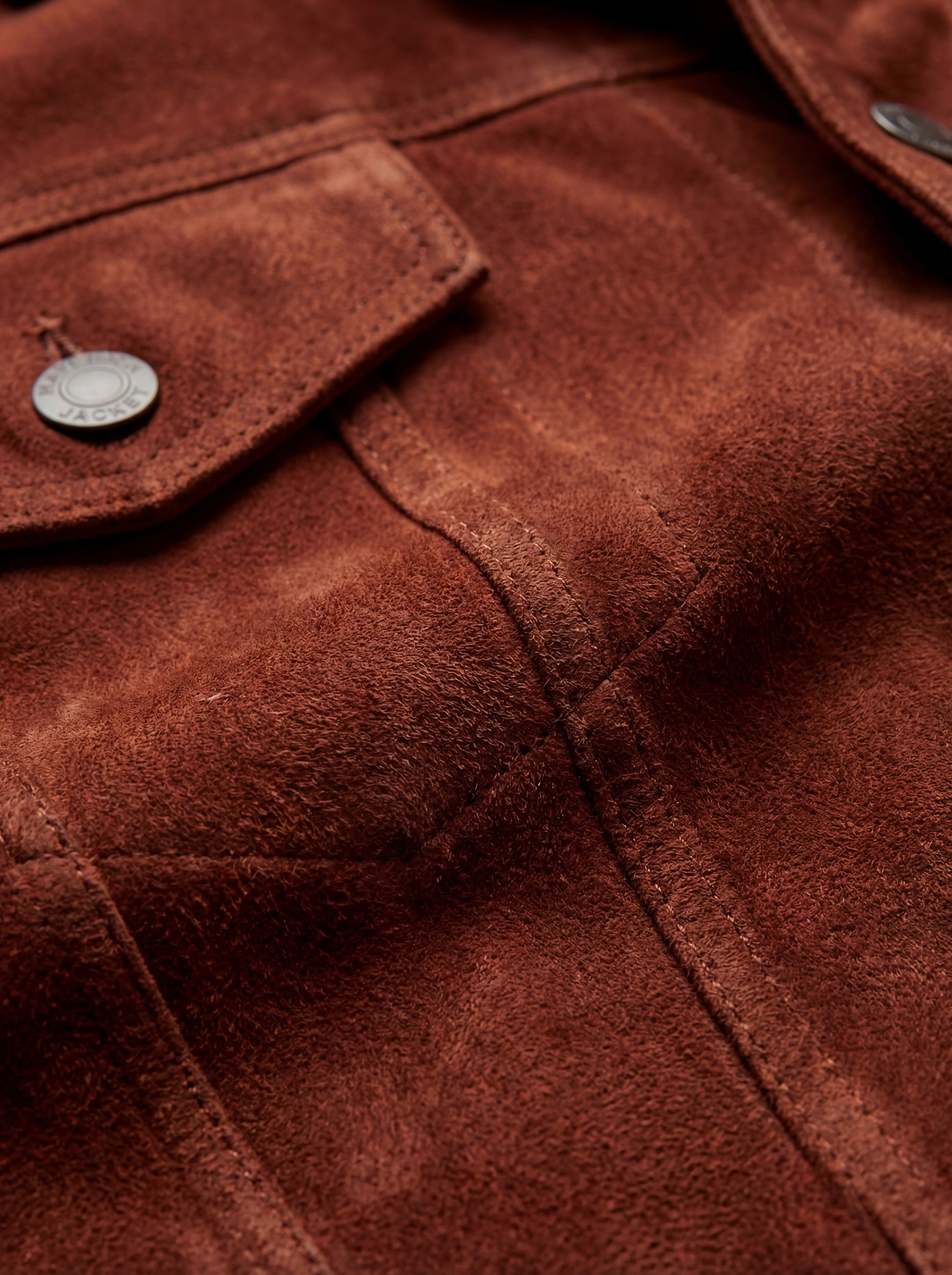 Macro shot of soft rust suede texture and silver hardware detail on trucker jacket. The Rowan by Maverick Jacket.