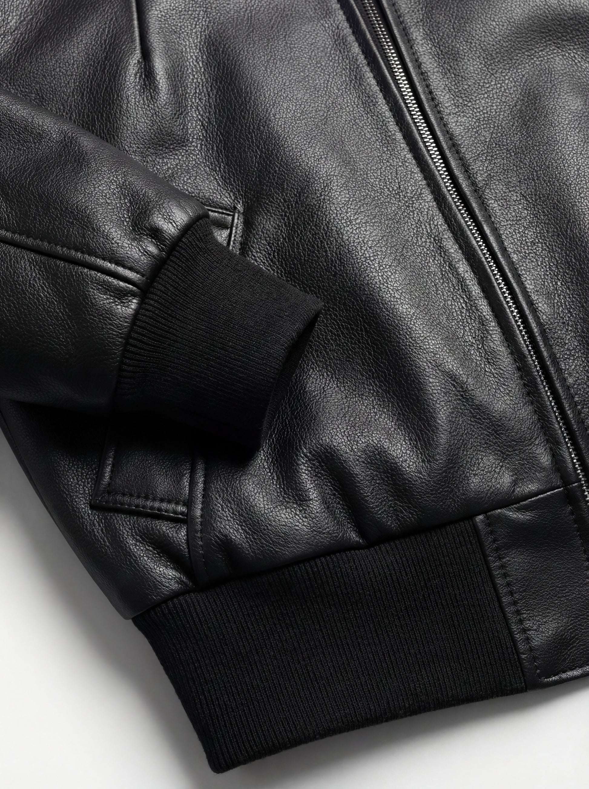 Macro shot of grained black leather texture and ribbed knit cuff detail on bomber jacket. The Isla by Maverick Jacket.
