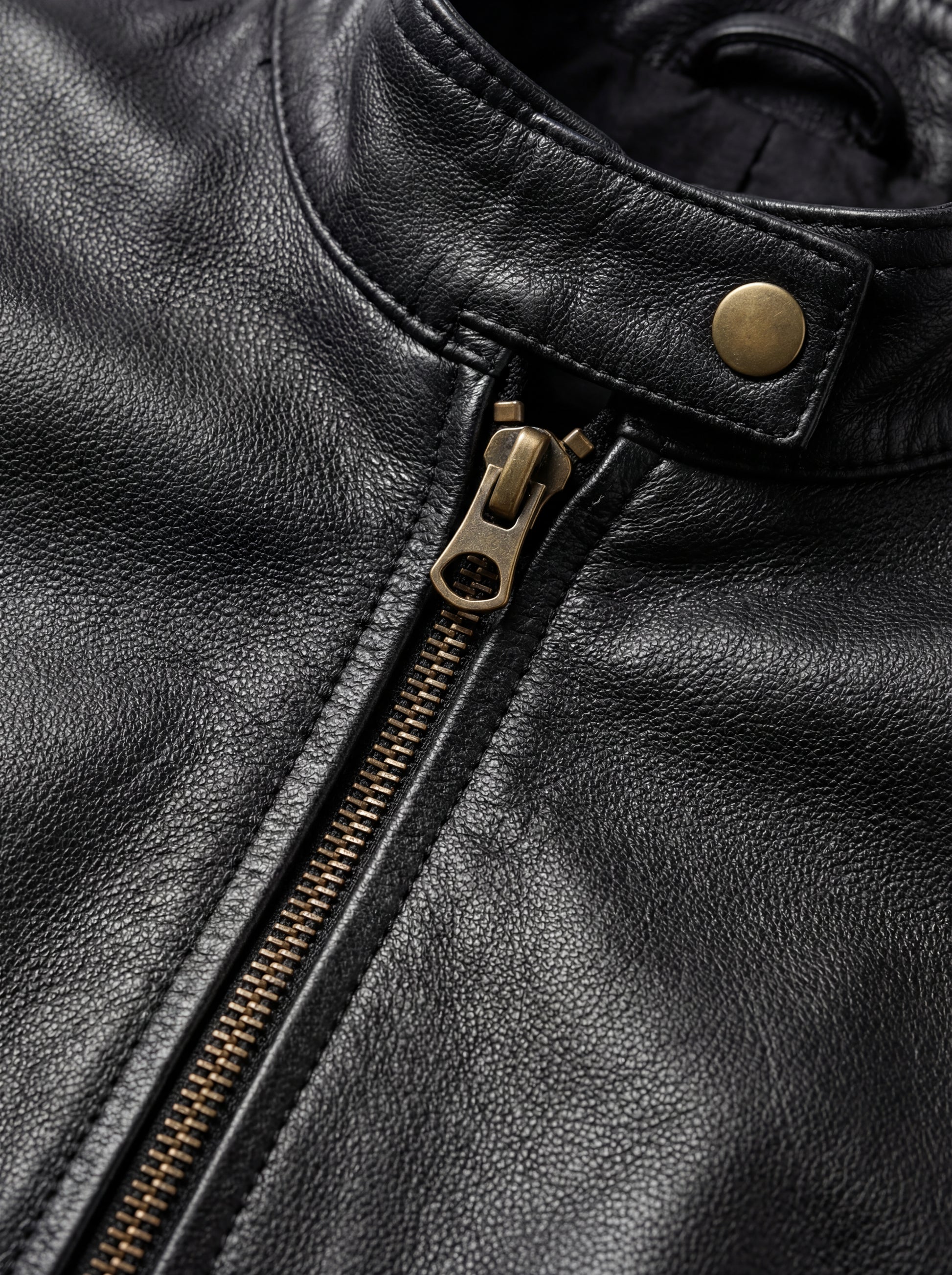 Macro shot of pebbled black leather texture and brass zipper puller on café racer jacket. The Maeve by Maverick Jacket.