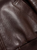 Macro shot of grained brown leather texture and tonal stitching detail on bomber jacket. The Isla by Maverick Jacket.