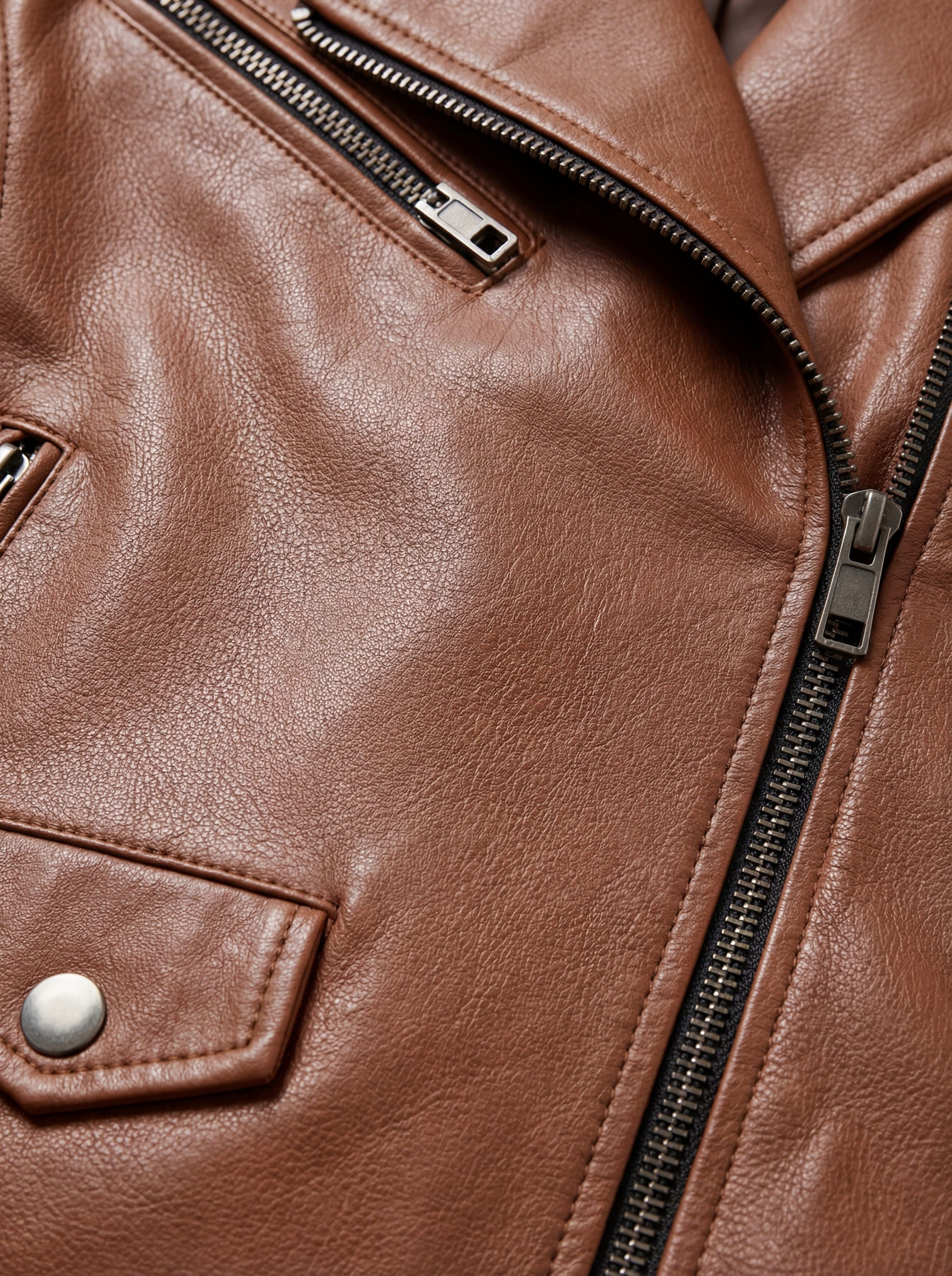 Macro shot of grained tan leather texture and silver zipper lapel detail on biker jacket. The Stella by Maverick Jacket.