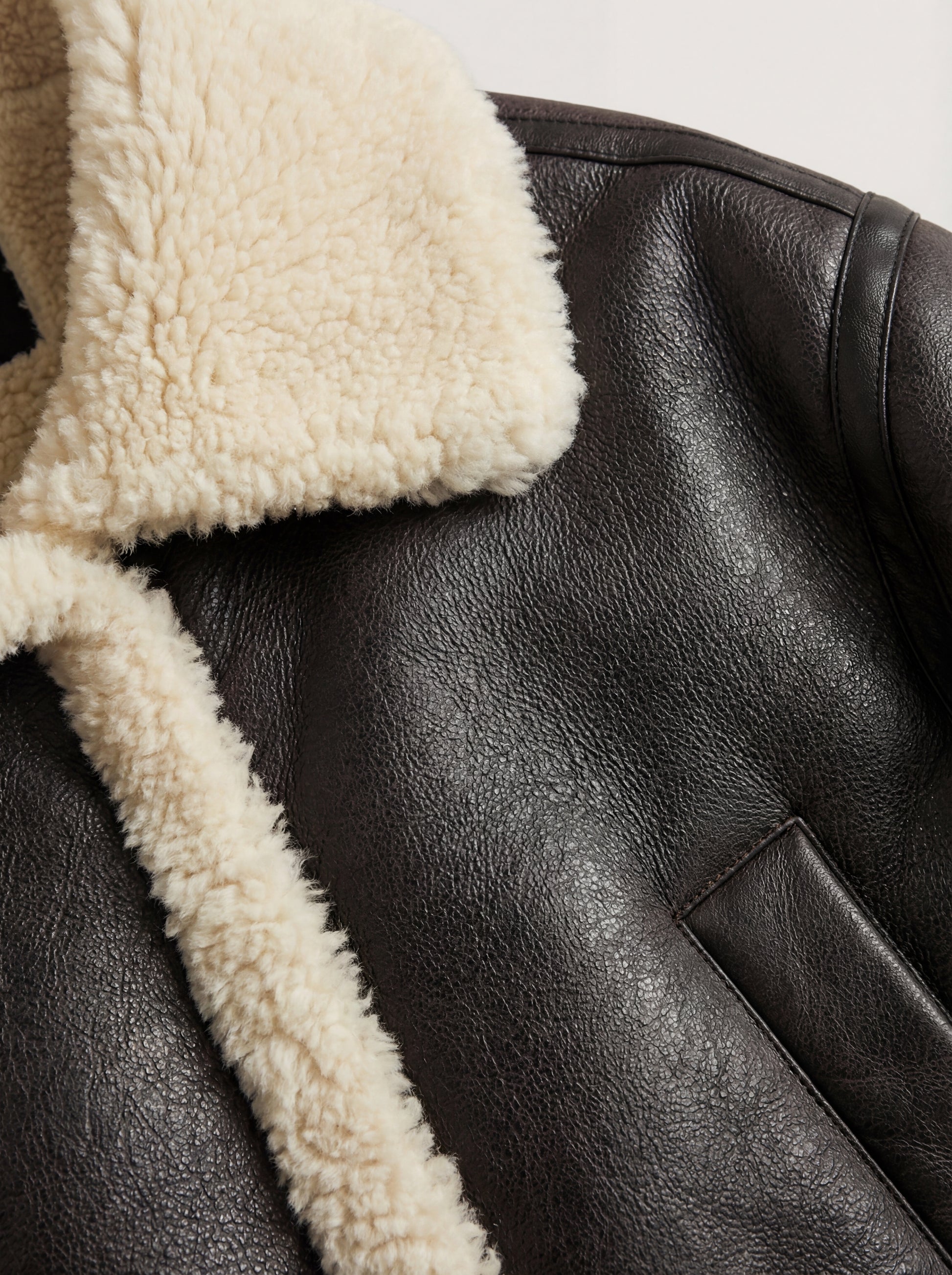 Macro shot of pebbled black leather grain and cream shearling fur texture on collar. The Thea by Maverick Jacket.