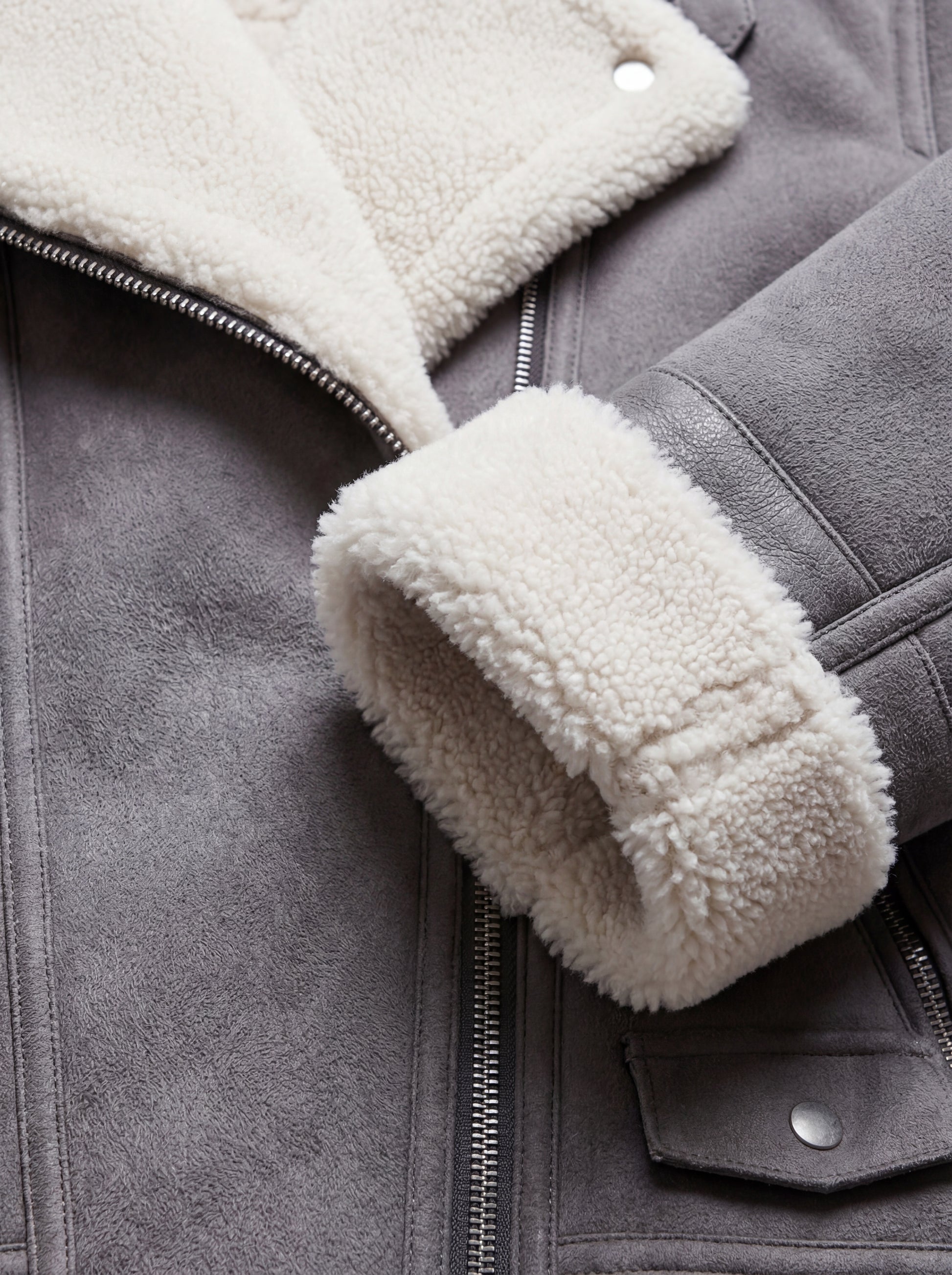 Macro shot of grey suede texture and thick white shearling cuff on aviator jacket. Maverick Esme.