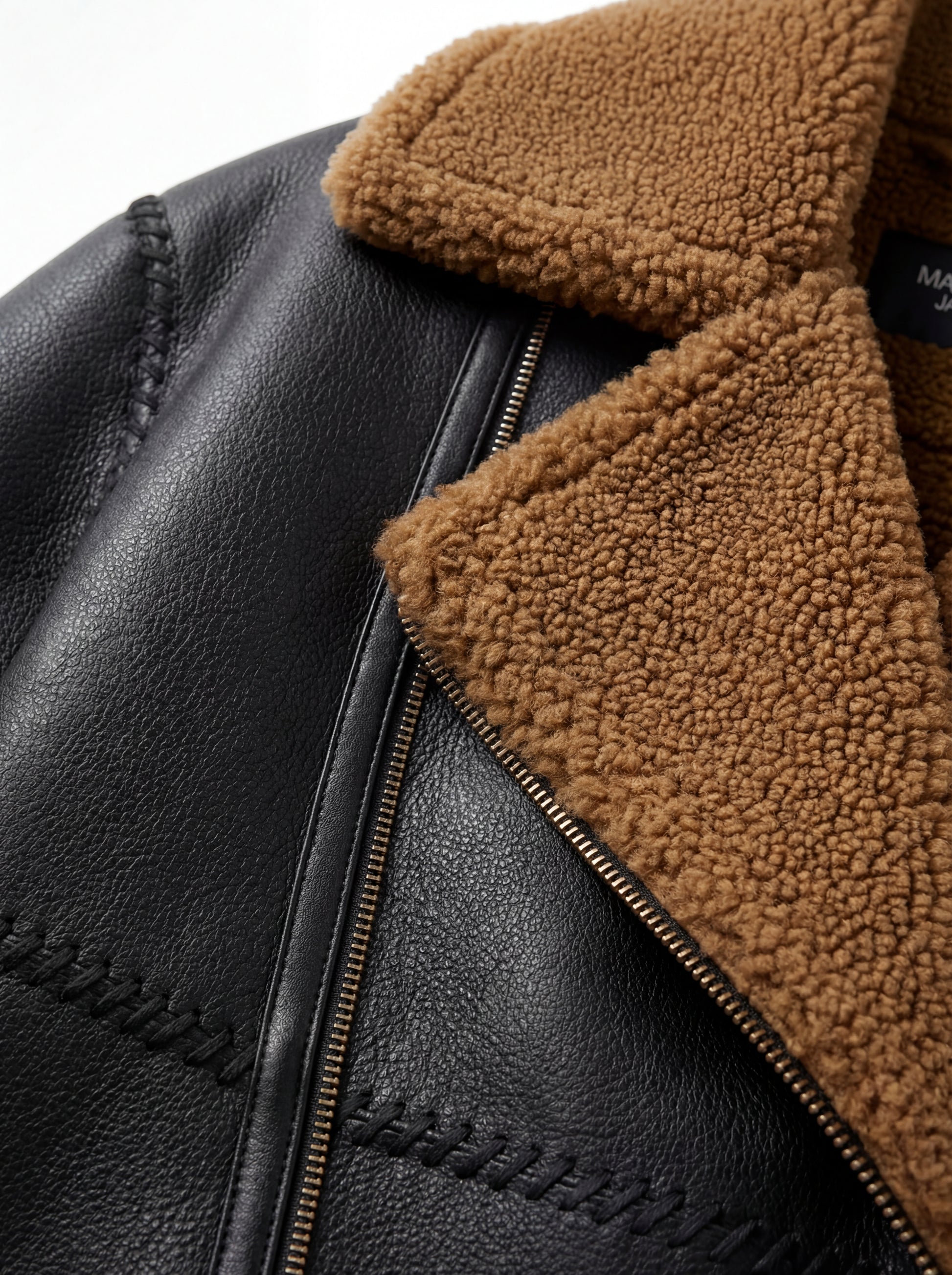 Macro shot of tan shearling texture and decorative braided leather stitching on jacket. Maverick Noa.