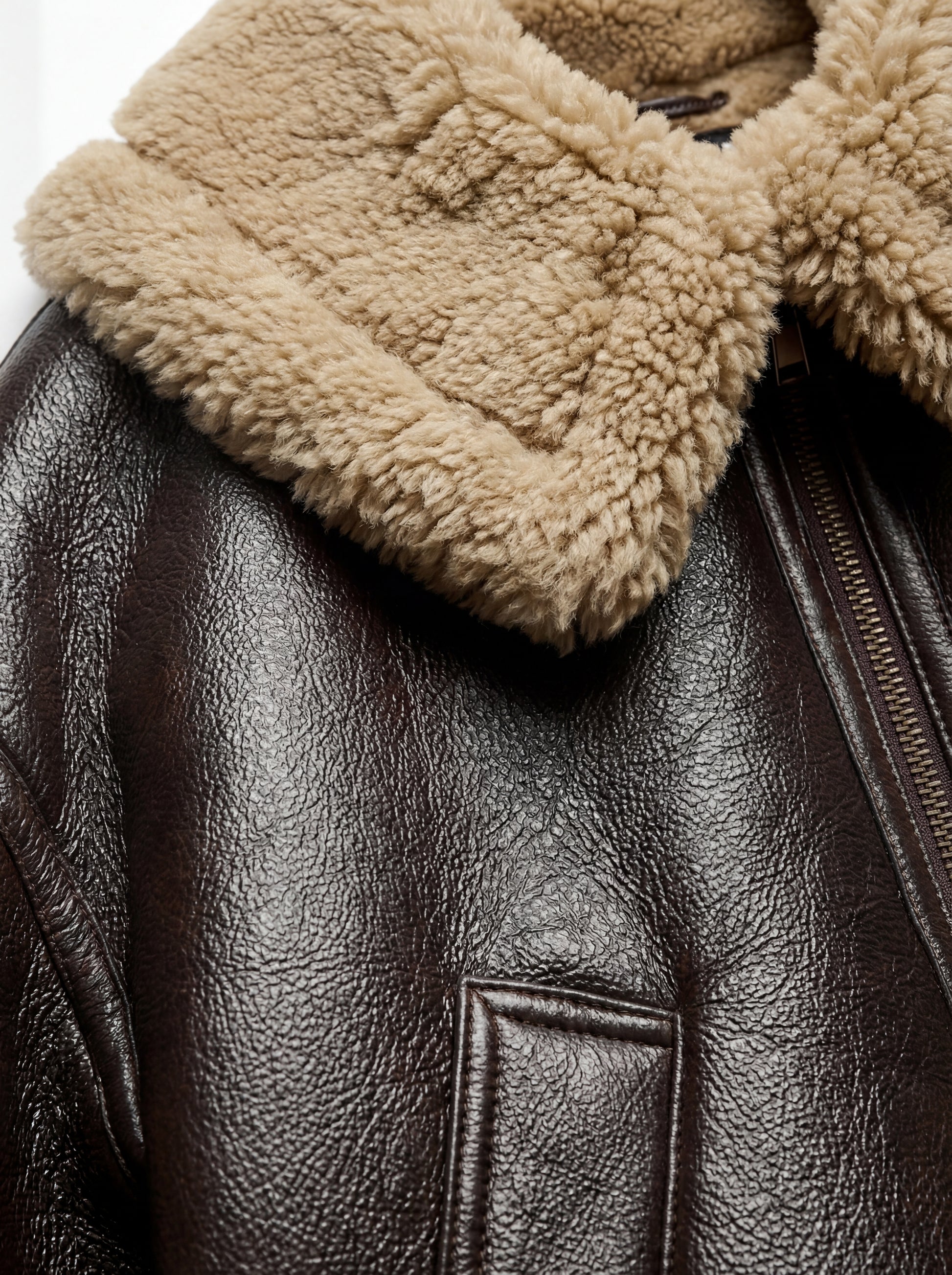 Macro shot of pebbled brown leather texture and fluffy beige shearling collar on jacket. Maverick Faye.