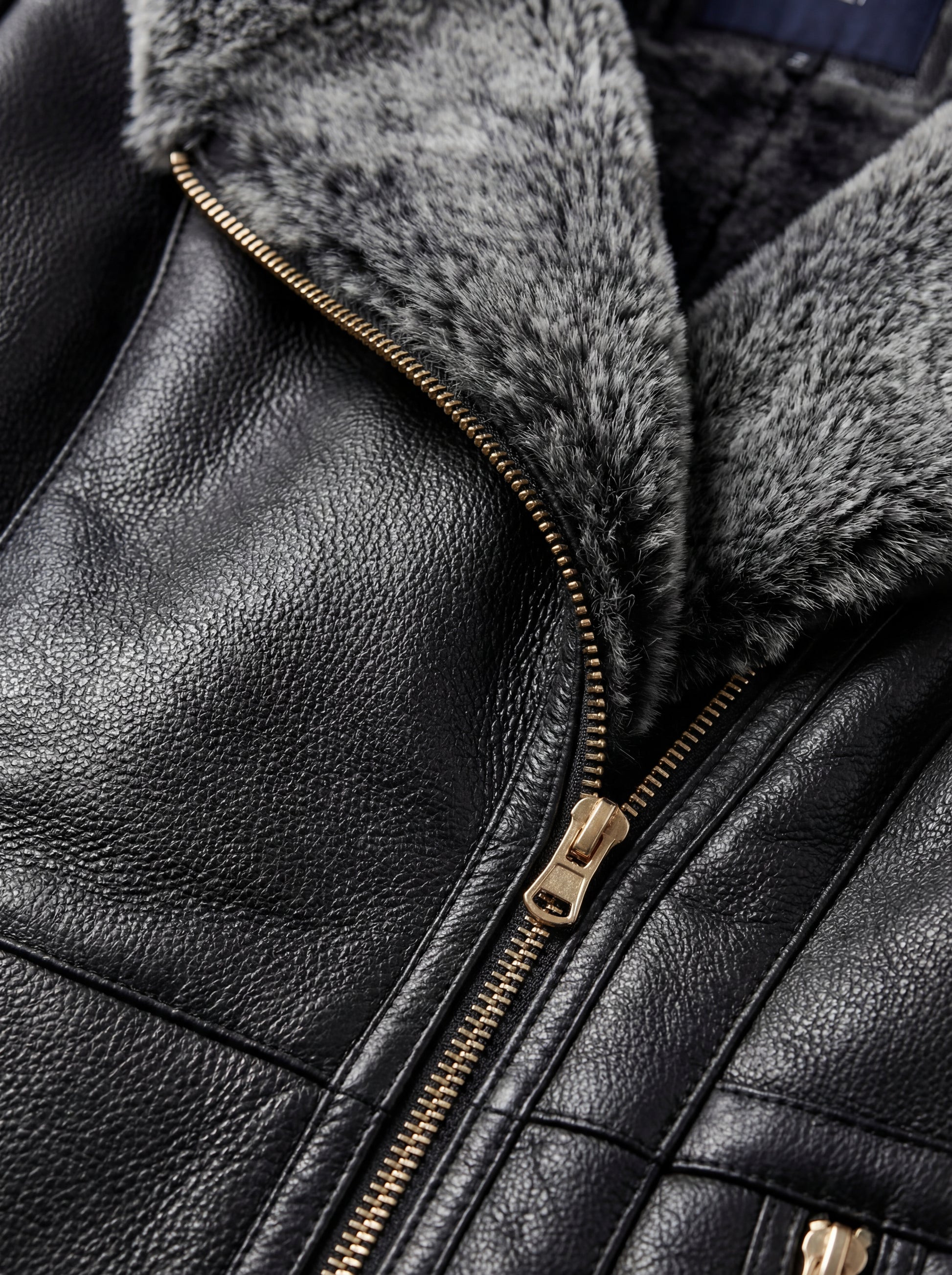 Macro shot of soft black leather texture contrasting with thick shearling wool and metal hardware on coat. The Genevieve by Maverick Jacket.