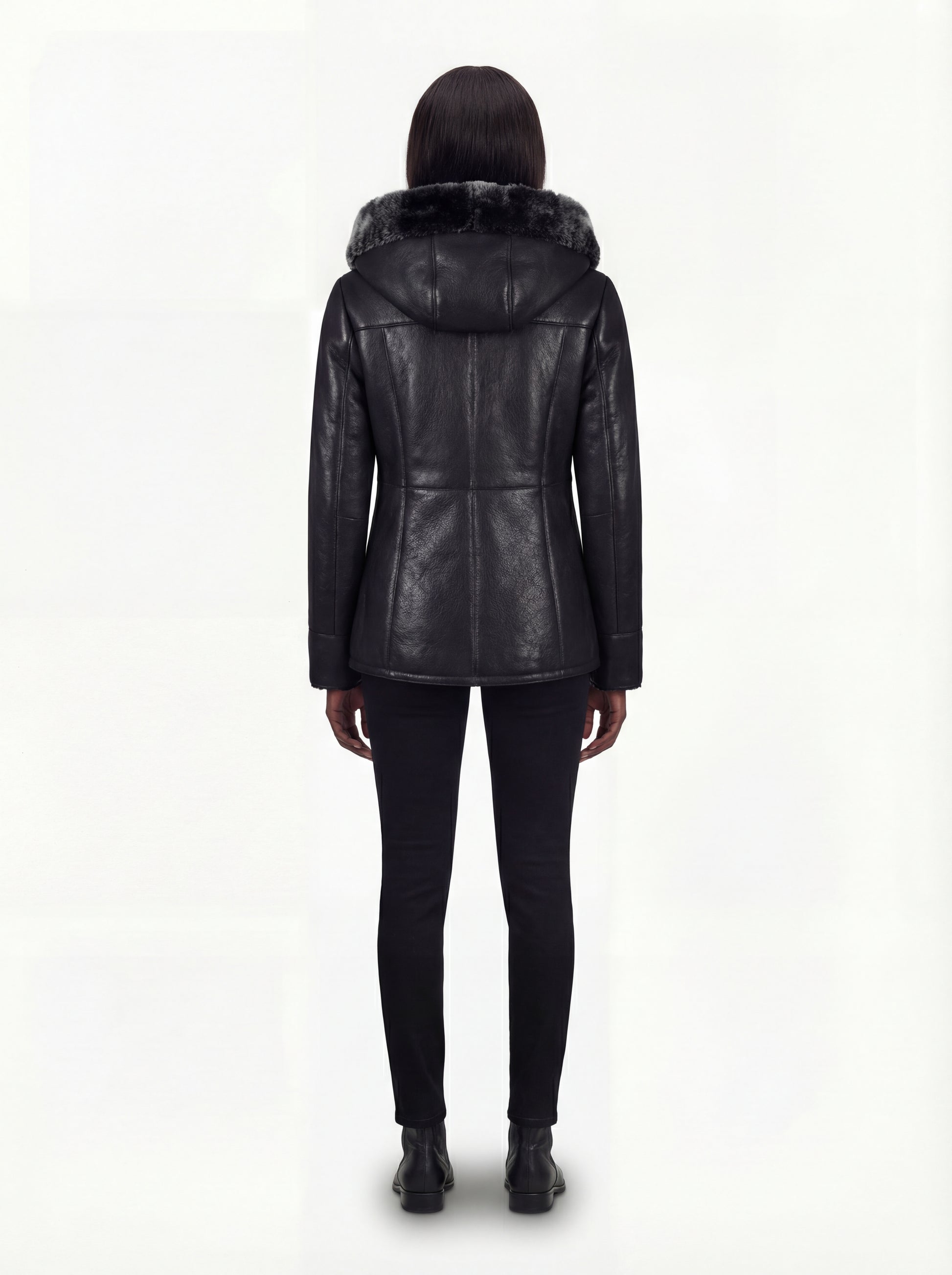Rear view of female model wearing Maverick Genevieve hooded shearling coat showing fitted shoulder drape and clean back styling. Maverick Jacket.