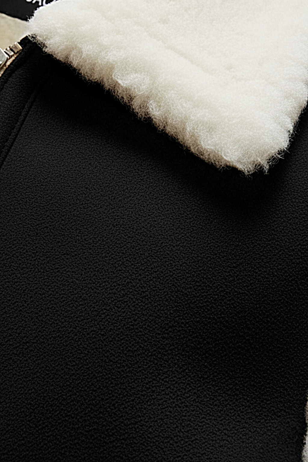 Macro shot of black nubuck texture and silver zipper hardware near cream wool collar on vest. The Elle by  Maverick Jacket.