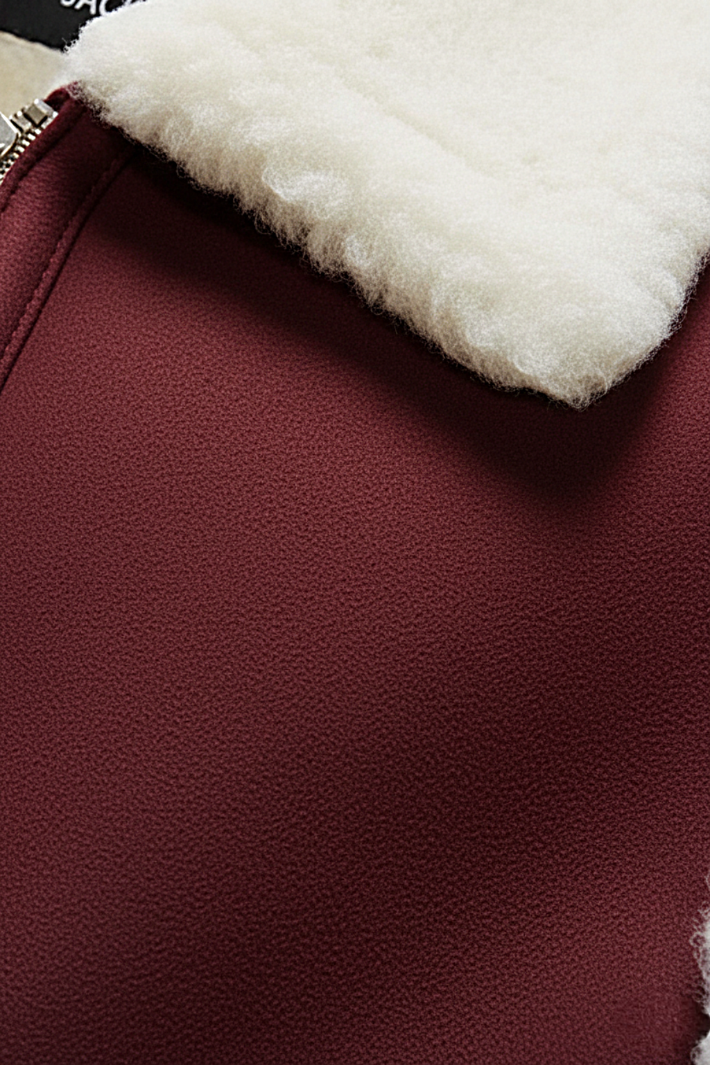 Macro shot of burgundy nubuck texture and silver zipper hardware near cream wool collar on vest. The Elle by Maverick Jacket.