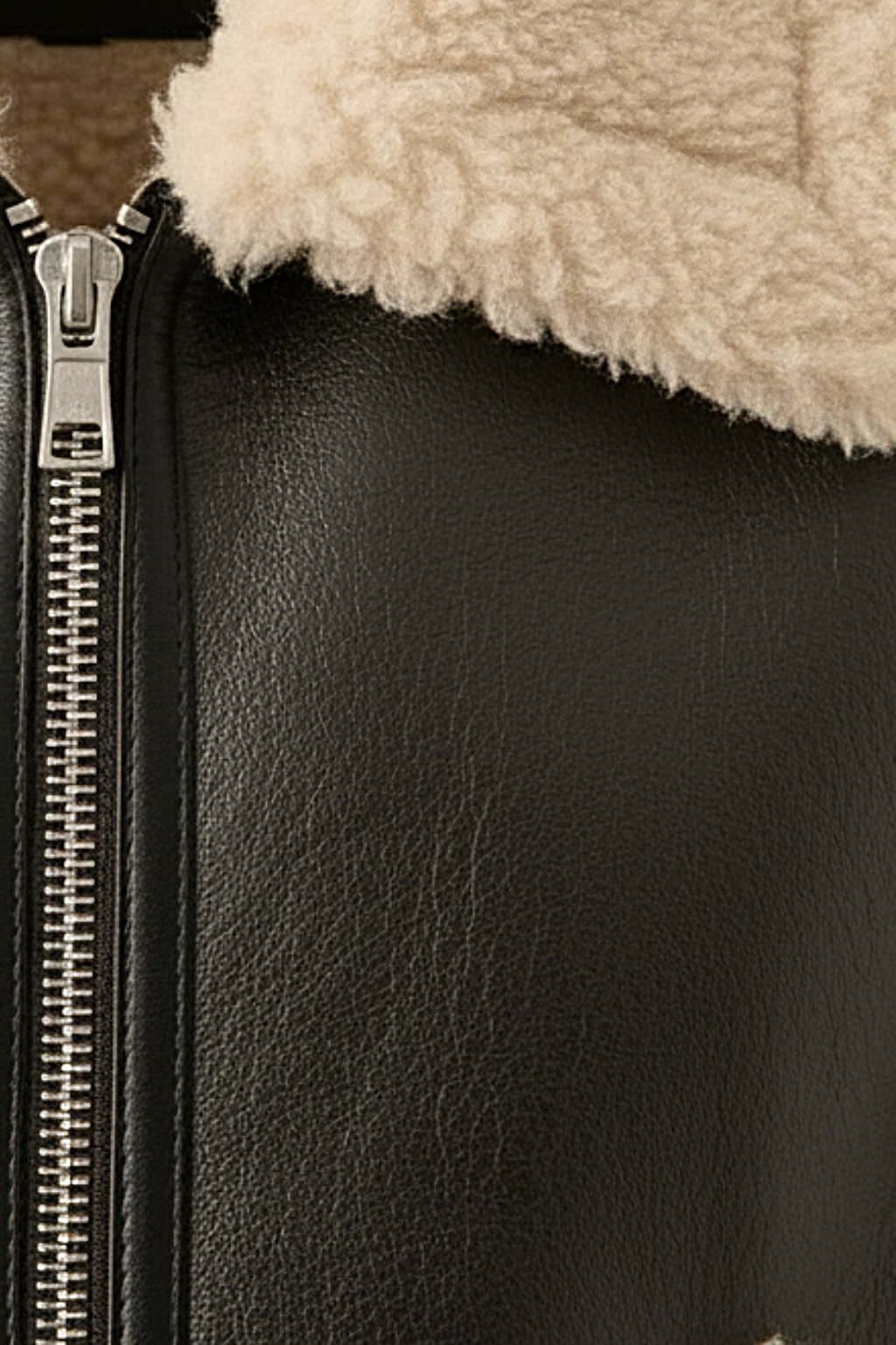 Macro shot of pebbled black leather texture and silver metal zipper hardware on shearling vest. The Clara by Maverick Jacket.