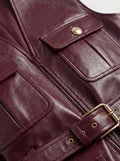 Macro shot of burgundy leather grain texture and gold embossed button detail on utility vest. The Victoria by Maverick Jacket.