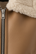 Macro shot of pebbled tan leather texture and silver metal zipper hardware on shearling vest. The Clara by Maverick Jacket.