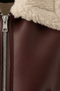 Macro shot of grained burgundy leather texture and silver zipper hardware on shearling vest. The Clara by Maverick Jacket.