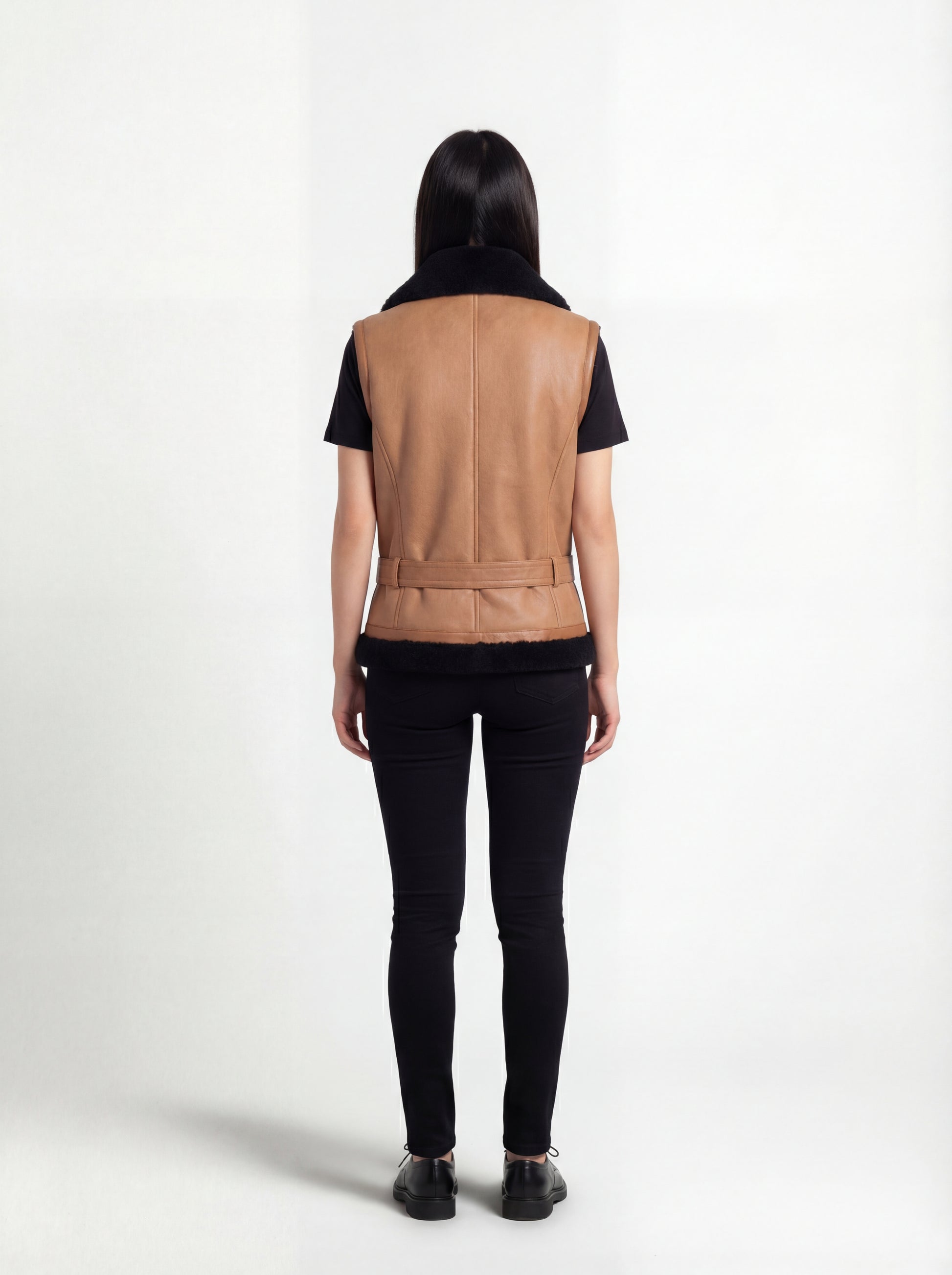 Rear view of female model wearing Maverick Valentina shearling vest showing structured back fit and belted hem styling. Maverick Jacket.