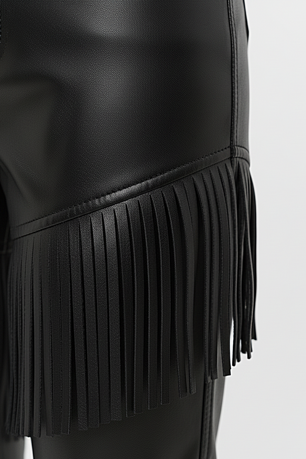 Macro shot of smooth black leather texture and precision-cut fringe detailing on pants. The Stevie by Maverick Jacket.