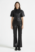 Female model wearing Maverick Bianca black leather flare pants, high-waisted fit, styled with matching black leather short-sleeve shirt and black leather boots. Maverick Jacket.