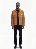 A man modeling a tan suede jacket over a black t-shirt and black pants, standing against a plain white studio background.