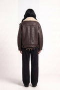 Back view of model in Maverick Taryn B-3 shearling bomber jacket, black tee, skinny black jeans and derby shoes; boxy fit.