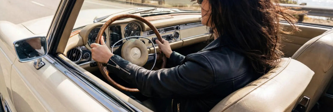 Person driving a classic car with a focus on the interior, wearing black leather jacket.